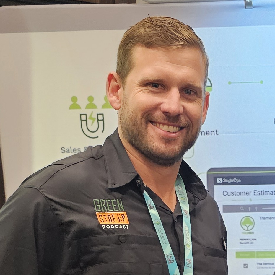 A person wearing a "Green Side Up Podcast" shirt stands in front of a banner displaying customer management software features at an event or expo.